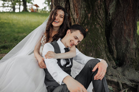 A beautiful bride with long curly hair in a chic dress hugs the groom, smiles, looking into the lens...