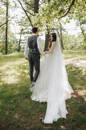 Stylish young brides, happy on their day, enjoy each other. They are walking in the spring park. Photo from the back. Spring wedding. Natural makeupの写真素材