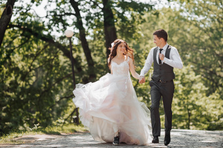 Groom and bride in the garden. Spring wedding in the park. Happy wedding couple running in the park. Stylish and beautiful. Princess dress.の写真素材