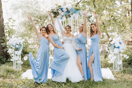 The bridesmaids in blue dresses raise their hands, rejoice, the bride is holding a beautiful bouquet. Beautiful luxury wedding blog concept. Spring wedding.の写真素材