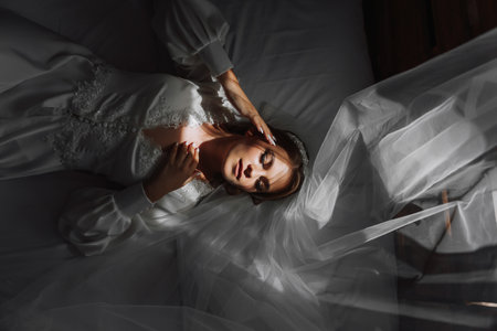 Beautiful young bride in a white peignoir lying on the bed in his bedroom. Last preparations for the wedding. The bride is waiting for the groom. Morning, the bride.の写真素材