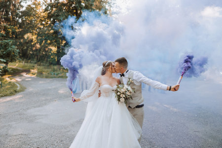In their hands, the newlyweds hold multi-colored smoke bombs of blue color. Groom and bride kiss. Wedding fun.の写真素材