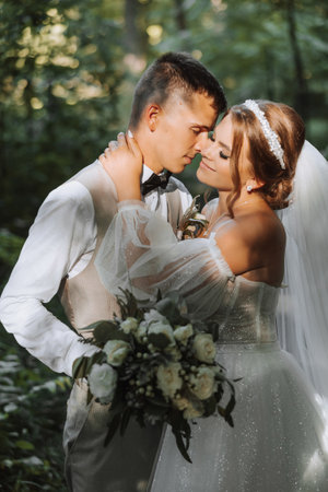 Portrait of a beautiful couple in love on wedding day. A walk in the park in the sunlight. Amazing kisses and hugs of the bride and groom with a bouquetの写真素材