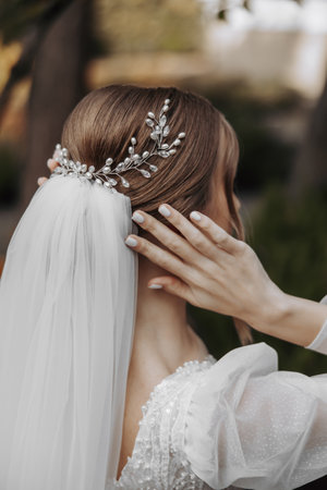 Hairstyle with an elegant wedding hair accessory. Photo from the back. Gently touches the veil. Beautiful and light dressの写真素材