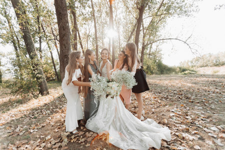 Wedding photo in nature. The bride and her bridesmaids are standing in the forest smiling, holding their bouquet and looking at the bride. Happy wedding concept. Emotions. girlsの写真素材