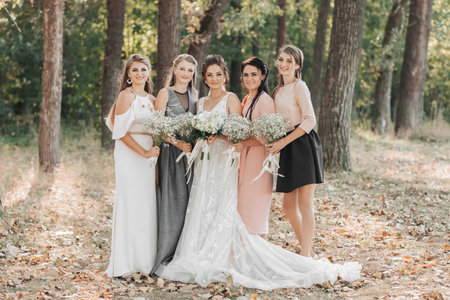 Wedding photo in nature. The bride and her bridesmaids are standing in the forest smiling, holding their bouquets and looking into the camera lens. Happy wedding concept. Emotions. girlsの写真素材