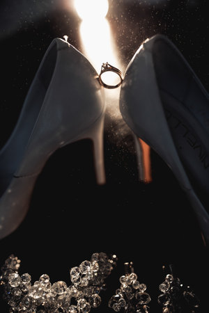 The bride's wedding ring stands on elegant white shoes in the backlight. Splashes of water on the shoes and wedding ring. Wedding photographyの写真素材