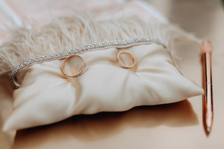 Wedding gold rings stand on a beige pillow decorated with feathers. Wedding accessories Preparation for the wedding ceremonyの写真素材