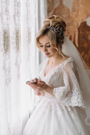 Wedding details. The bride in a white dress holds the groom's wedding boutonniere and looks at it. Beautiful hands. French manicure. Beautiful hair and makeupの写真素材