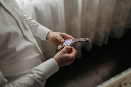 Details. A man in a white shirt holds a watch with both hands. Fashion and style. Business. Men's...