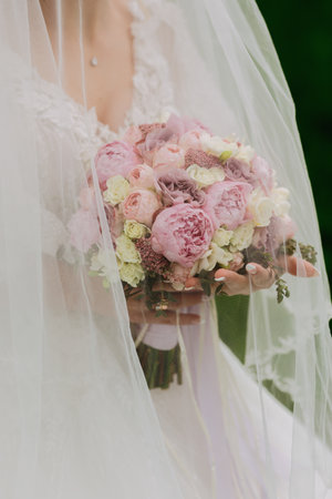 Photo of a bouquet of pink peonies. The bride is standing with a bouquet in a white dress covered with a veil. A wonderful dress. Pretty Woman. Wedding photoの写真素材