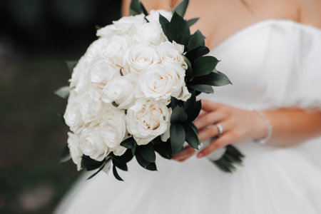 Cropped photo. The bride is wearing a white dress with a neckline, holding a bouquet of white roses. Beautiful hands and silver jewelry. French manicure. Portrait of the bride.の写真素材