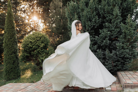 Wedding photo. The bride in a voluminous white dress and a long veil, smiling, twirling with a...