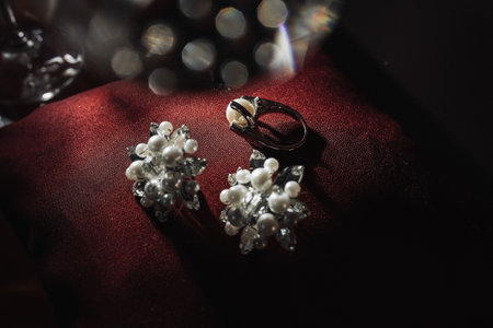 Silver bridal engagement ring with pearl and silver earrings with pearls on a red background. Beautiful light. Photo of wedding details.の写真素材