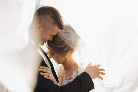 Wedding portrait. The groom in a black suit and the blonde bride are hugging, wrapped in the bride's...