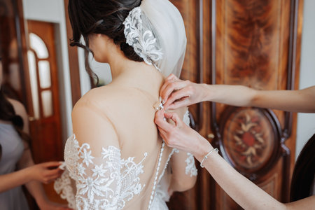The bride's friends fasten the white voluminous dress of the bride. Rear view. Open shoulders....