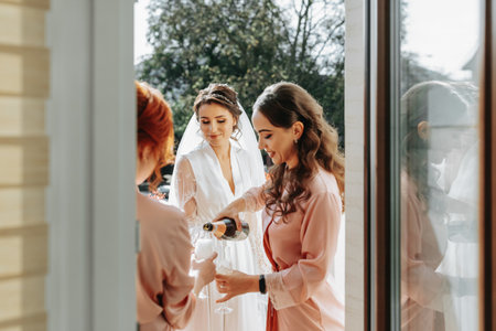 Young bridesmaids are having fun and smiling in pink silk robes drinking champagne at the bride's gazebo. Beautiful women celebrate a bachelorette party, in a gazebo and with champagne.の写真素材