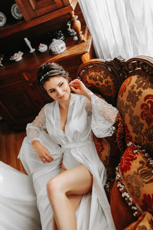 beautiful bride on a retro sofa in a robe with open legs, full length photo. Wedding hairstyle, light makeupの写真素材
