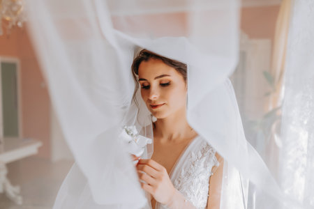 A brunette bride in a white dress holds her wedding bouquet, poses. French manicure. Open shoulders. Beautiful hands. Long veil. Morning of the bride. Detailsの写真素材