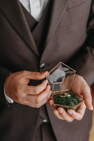 Wedding gold rings on a decorative glass box with wooden green moss, standing in the hands of the...