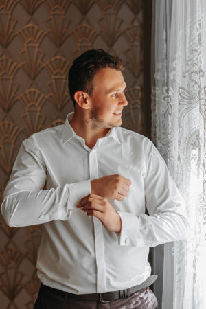 Portrait of a fashionable man fastening stylish cufflinks on the sleeves of his white shirt. Wedding...