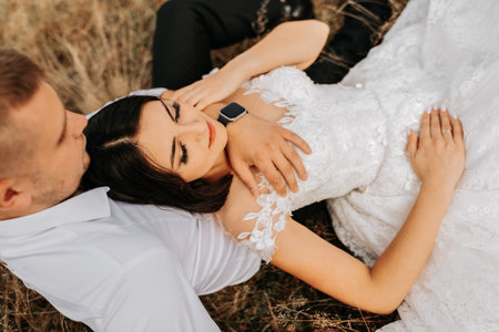 The bride and groom are lying on the dry grass and hugging, a woman in a white wedding dress. Beautiful autumn wedding photo.の写真素材