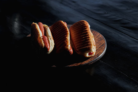 Three delicious, freshly prepared hot dogs displayed on a black wooden stand. Concept for a picnic or barbecue with family and friends. High quality photoの写真素材