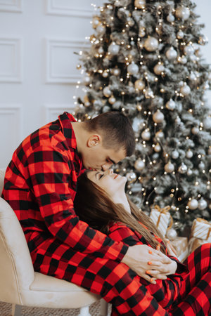 Young beautiful couple in matching red pajamas near the Christmas tree. Joy, hugs and kisses. New Year's holidays and gifts under the Christmas treeの写真素材