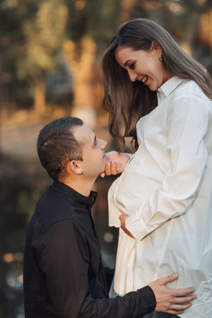 young pregnant woman in a white shirt. The husband put his hands on his wife's stomach and leaned against his ear.の写真素材