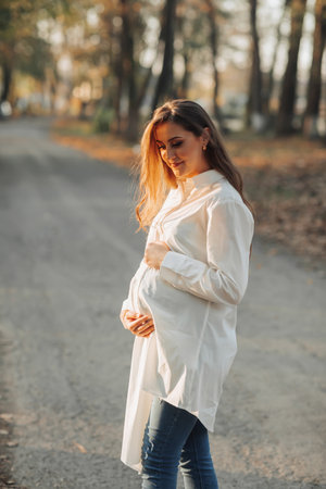 Portrait of a happy and beautiful pregnant woman looking at the light in the park at sunset. The beauty of a woman during pregnancy. How to be happy and healthy in autumn. Autumn mood.の写真素材