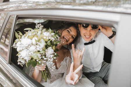 young happy bride and groom are rejoicing after the wedding ceremony in their carの写真素材