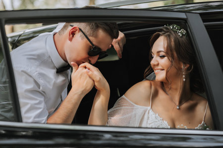 Wedding portrait, photo of a stylish groom in a white shirt and bow tie and a brunette bride with a bouquet of flowers near a black car.の写真素材