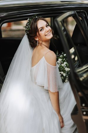 A beautiful bride in a white dress with a bouquet poses near a car in nature. Wedding portrait of a cute girl. Photography and concept.の写真素材