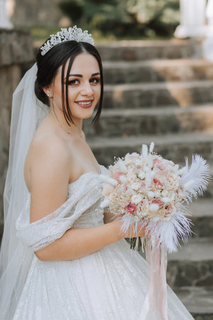 wedding bouquet of pink roses, feathers and dried flowers in the hands of the brideの写真素材