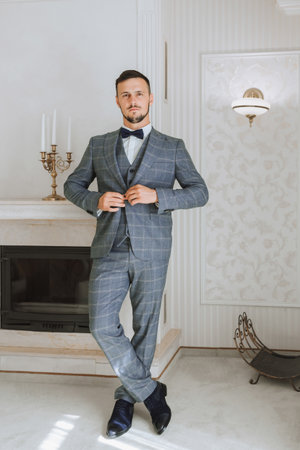 A stylish groom with a beard is preparing for the wedding ceremony. Groom's morning. A businessman fastens his jacket. The groom is getting ready in the morning before the wedding ceremonyの写真素材