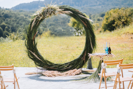 The wedding arch in the park is made of dry reeds on the background of the forest in blurred focus. Away wedding ceremony. Decorated chairs for the ceremonyの写真素材