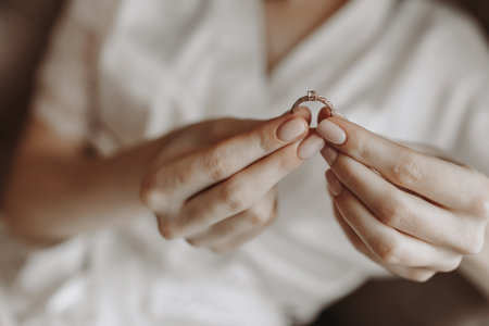 Close up of a gold ring with a diamond in a woman's fingers with a French manicure. Love, relationship and wedding concept. Soft and selective focus. Free spaceの写真素材