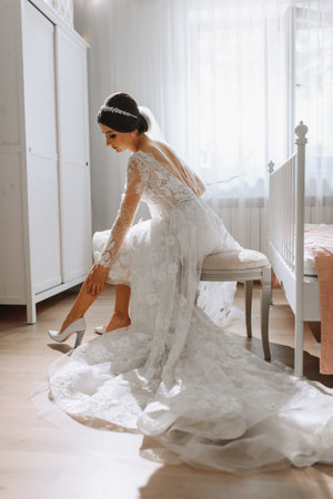 A beautiful young bride in a white wedding dress puts on shoes. Final preparations for the wedding. The bride is waiting for the groom. Morning, bride.の写真素材