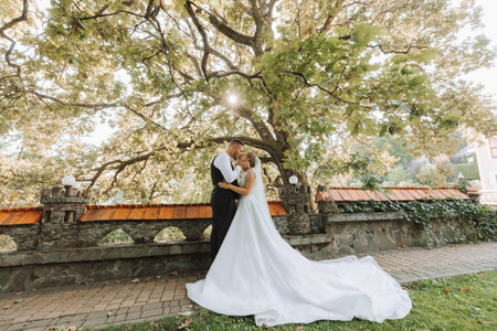 The bride and groom are standing and embracing in a beautiful yard. Wide angle photo of the sunset.の写真素材