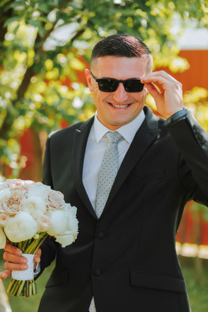 Photo of the groom in a classic black suit and glasses, with a bouquet of flowers in his handsの写真素材