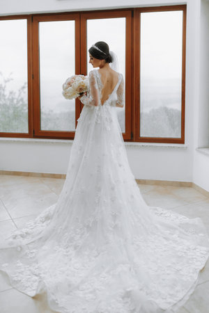 Very nice young woman in white dress holding beautiful tender blooming bouquet of fresh white and pink peony flowersの写真素材