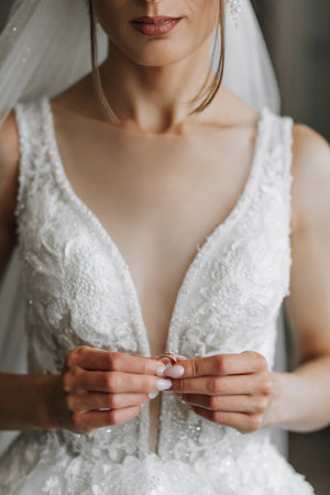 bride holding a wedding ring, close-up. French manicure. Wedding dress with a deep necklineの写真素材