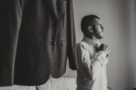 The groom buttons up his white shirt before changing into his formal attire. Suit of the groomの写真素材