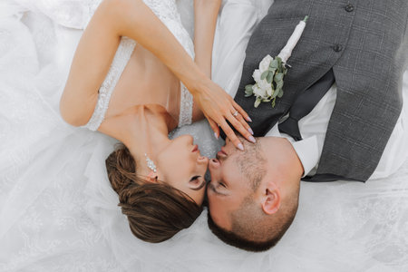 beautiful fabulous happy bride and stylish groom lie on the bride's white wedding dressの写真素材