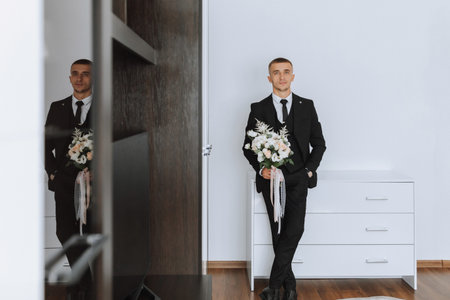 portrait. A man in a white shirt, black suit poses in a white room, holding a bouquet. A stylish watch. Men's style. Fashion. Businessの写真素材