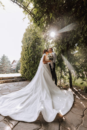 portrait of the bride and groom in the park, the bride and groom are hugging and tenderly kissing. Wedding walk in the park. Long train of the dressの写真素材