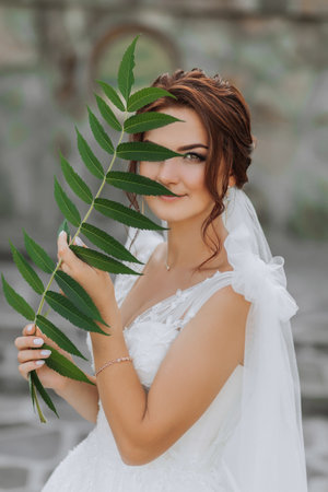 Wedding portrait. The bride in a white dress is posing, holding a leaf near her face and looking into the lens. Nice makeup. Portrait of the brideの写真素材