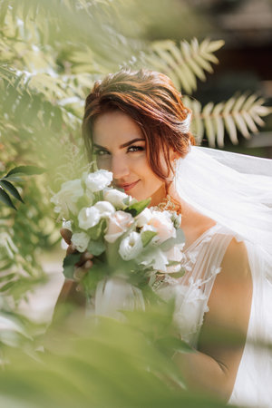 Wedding portrait. The bride in a white dress with a veil in the air, posing near a coniferous tree. The curtain is in the air. Open shoulders of the bride. Photo session in nature.の写真素材