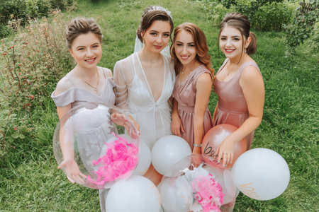 The bridesmaids look at the smiling bride. The bride and her fun friends celebrate a bachelorette party outdoors in matching dresses. The bride and friends on the grass under the open skyの写真素材