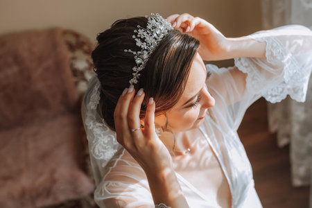 a beautiful bride in a white robe with an open bust and a crown on her head. The bride is preparing for the wedding. bride's fees the wedding day of the newlyweds.の写真素材